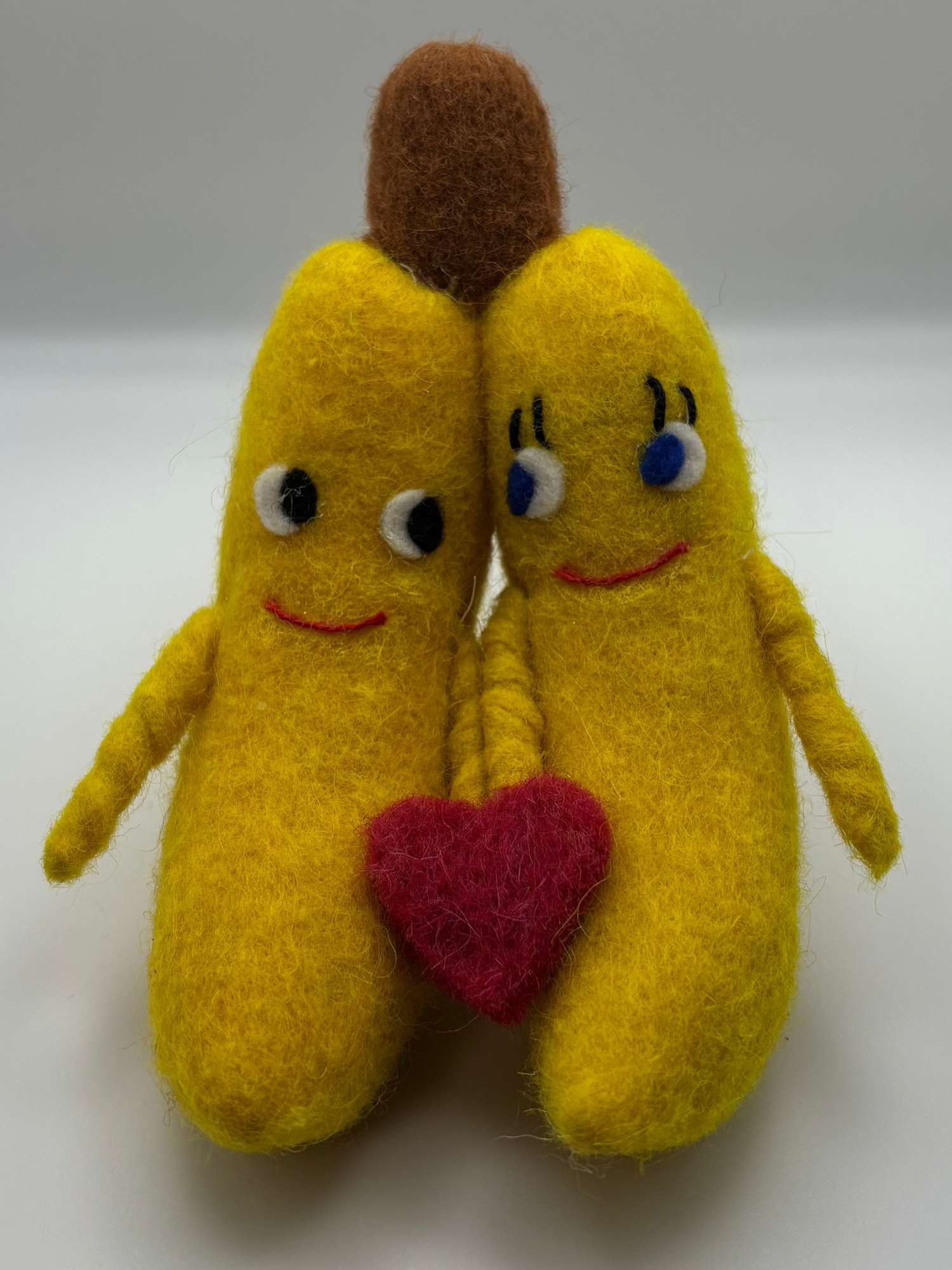 Two plush banana toys with a heart between them on a white background